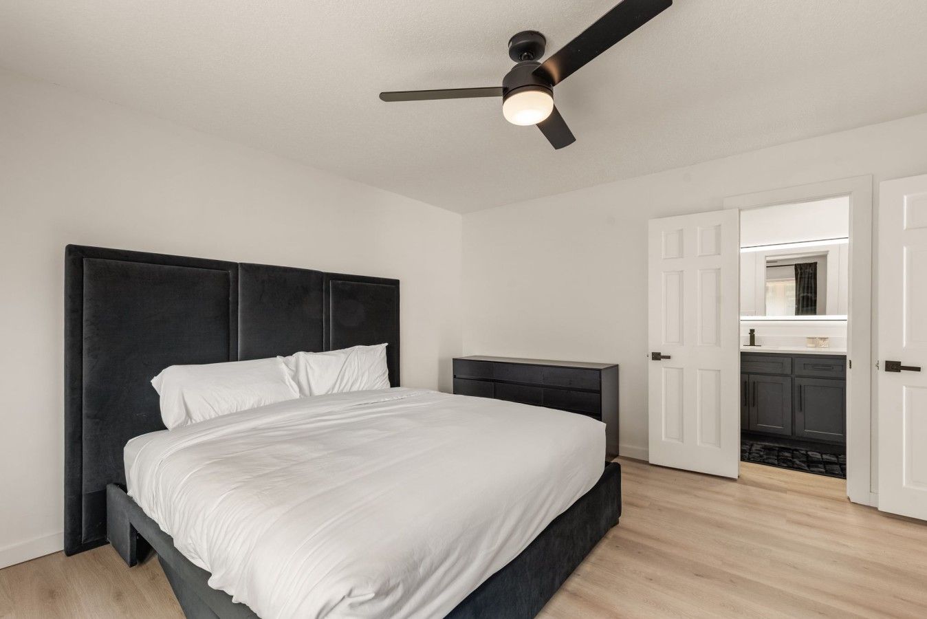 A bedroom with a bed, bedside tables, a ceiling fan, and an open door leading to a bathroom.