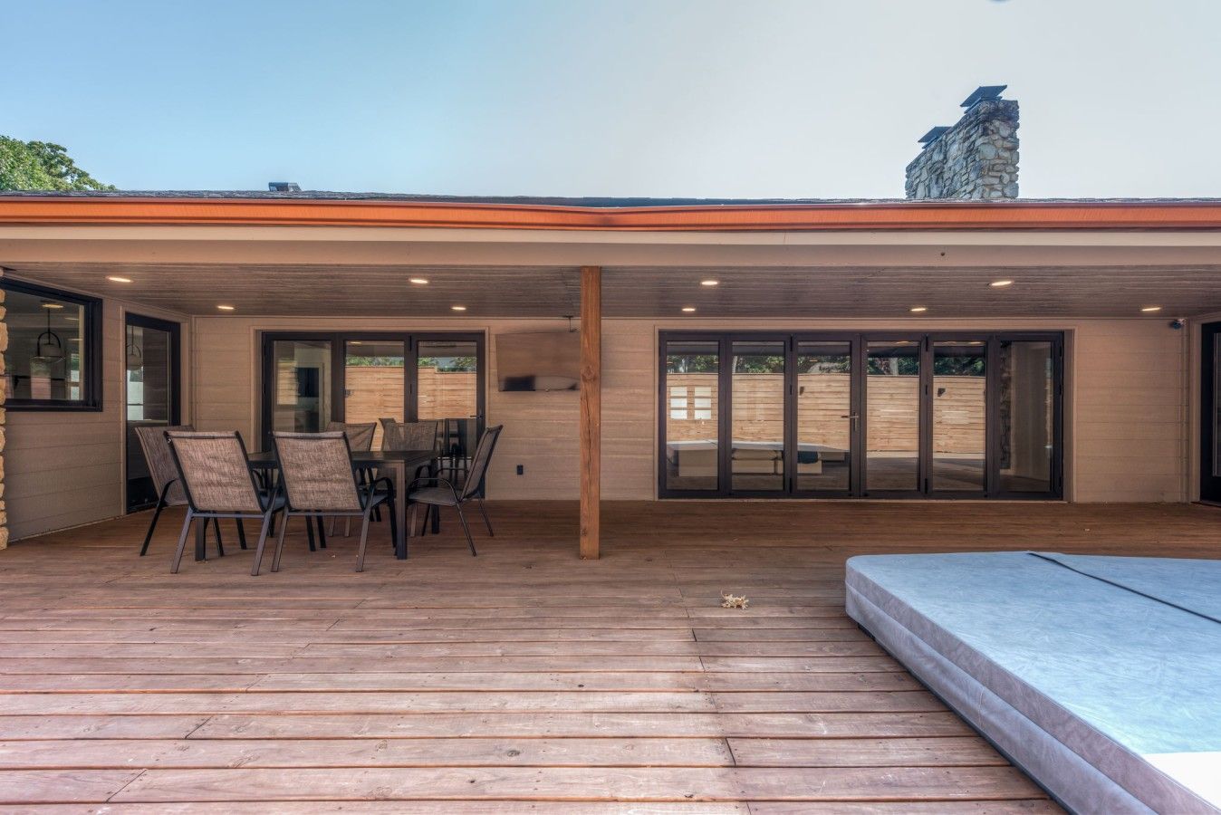 A covered patio with a dining table and chairs, a wooden deck, and a stone chimney.