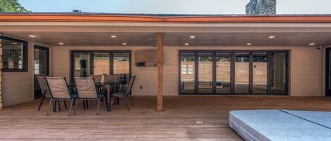 A covered patio with a dining table and chairs, a wooden deck, and a stone chimney.