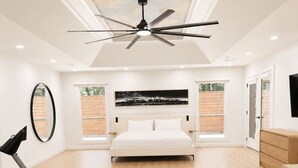 A spacious bedroom with a large bed, a ceiling fan, and a view of the outdoors through a window. - Luxury South Tulsa Retreat | 4 King Beds • Hot Tub (Tulsa)