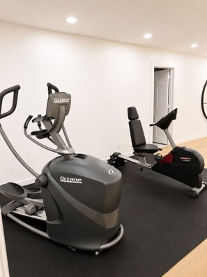 An indoor gym with two stationary bikes and a door leading to another room. - Luxury South Tulsa Retreat | 4 King Beds • Hot Tub (Tulsa)