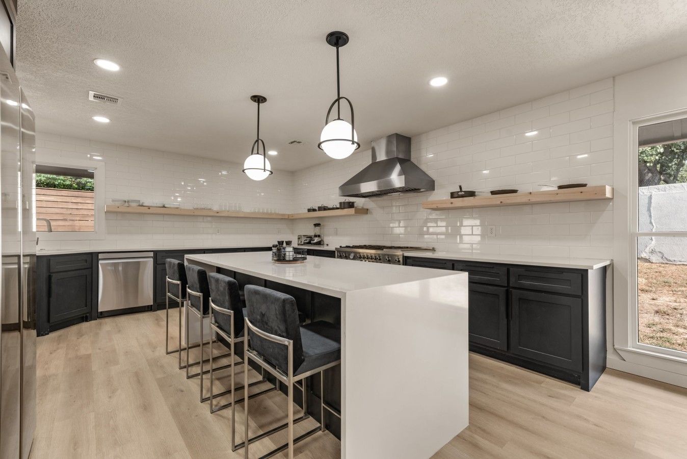 A modern kitchen with a central island, bar stools, and a large window.