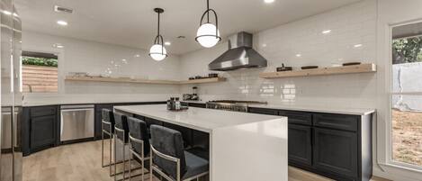 A modern kitchen with a central island, bar stools, and a large window.