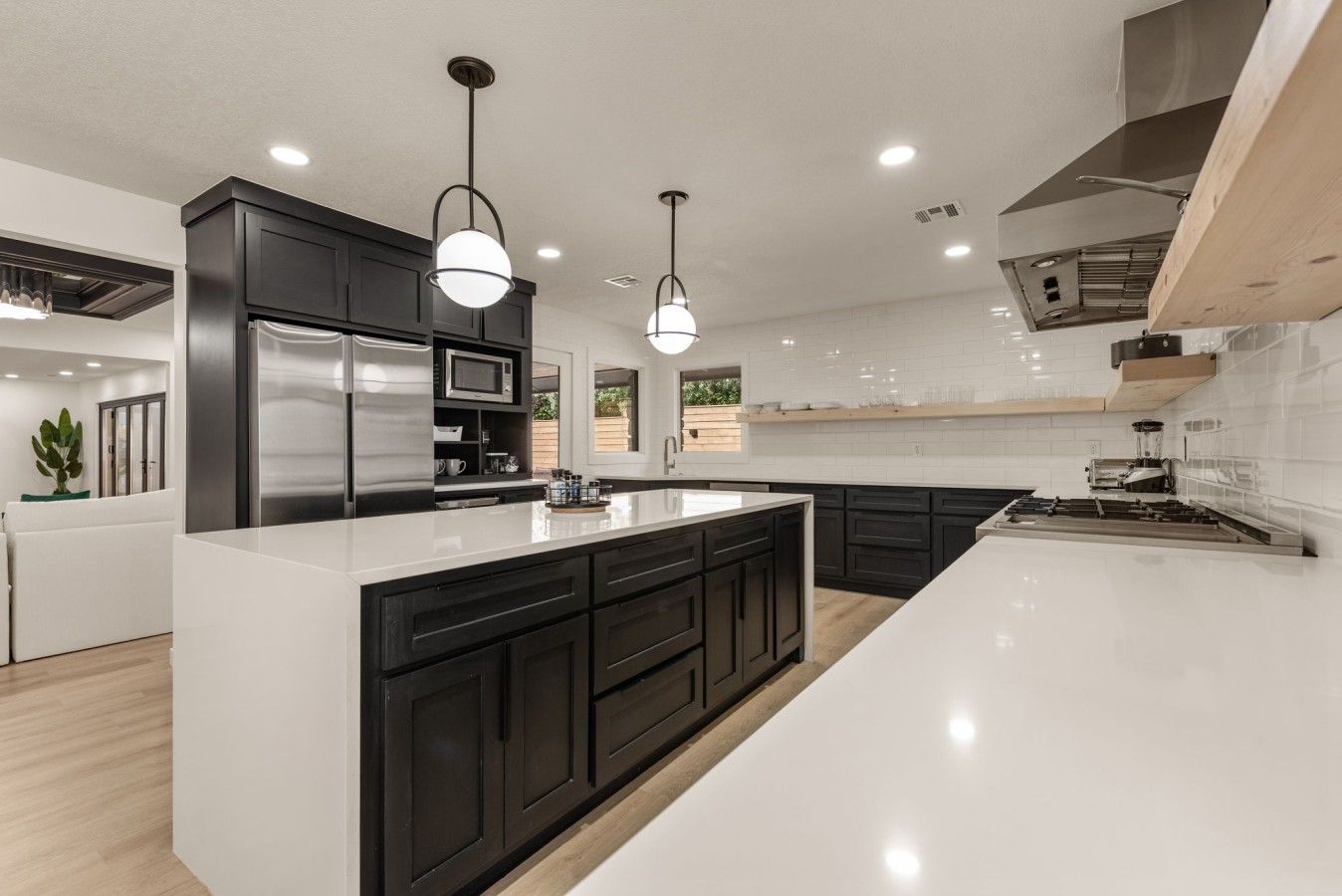 A modern kitchen with a large island, dark cabinetry, stainless steel appliances, and pendant lighting.
