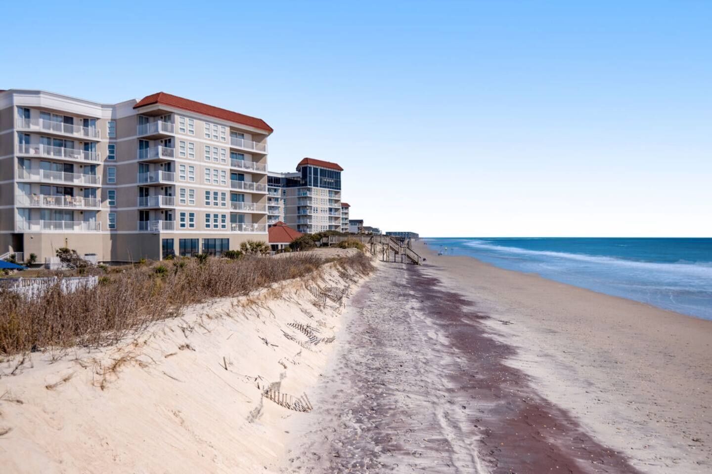 A beachfront hotel with multiple floors, balconies, and a sandy beach.