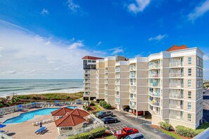 Ein mehrstöckiges Hotel mit Schwimmbad, Blick auf den Strand und Parkplatz.
