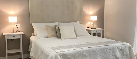 Un dormitorio con una cama grande, dos mesitas de noche, aire acondicionado de pared y una lámpara de noche.