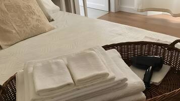 A neatly made bed with a stack of folded towels and a hairdryer in a wicker basket.