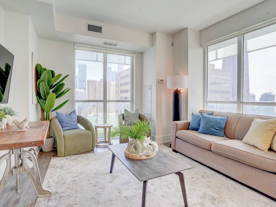 A modern living room with a sofa, armchairs, a coffee table, and large windows.