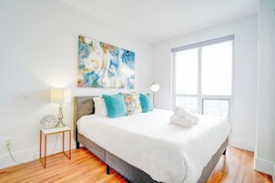 A modern bedroom with a large bed, a nightstand with a lamp, and a wall-mounted painting.