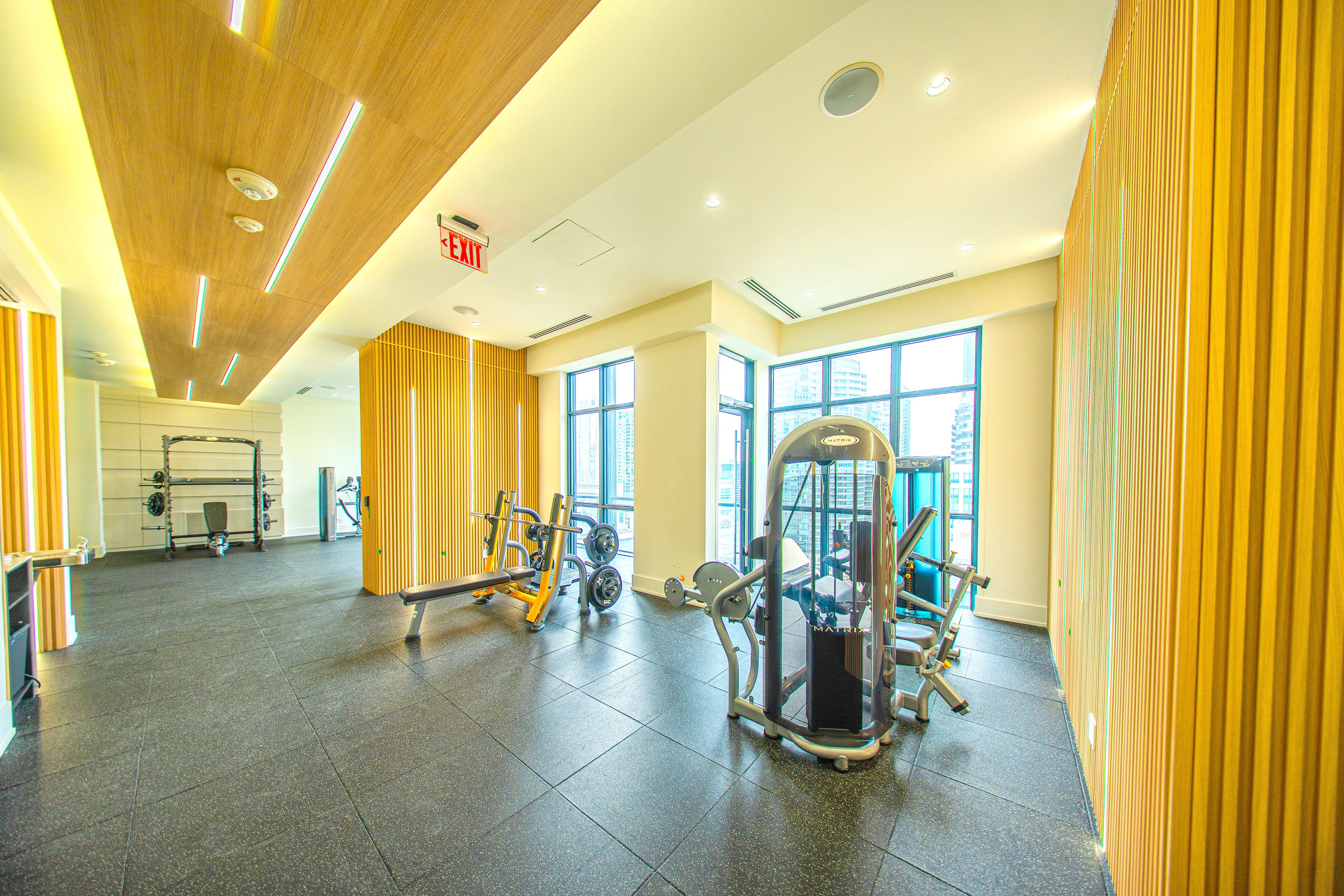 Un gimnasio con equipamiento de ejercicio, ventanas amplias y techo de madera.