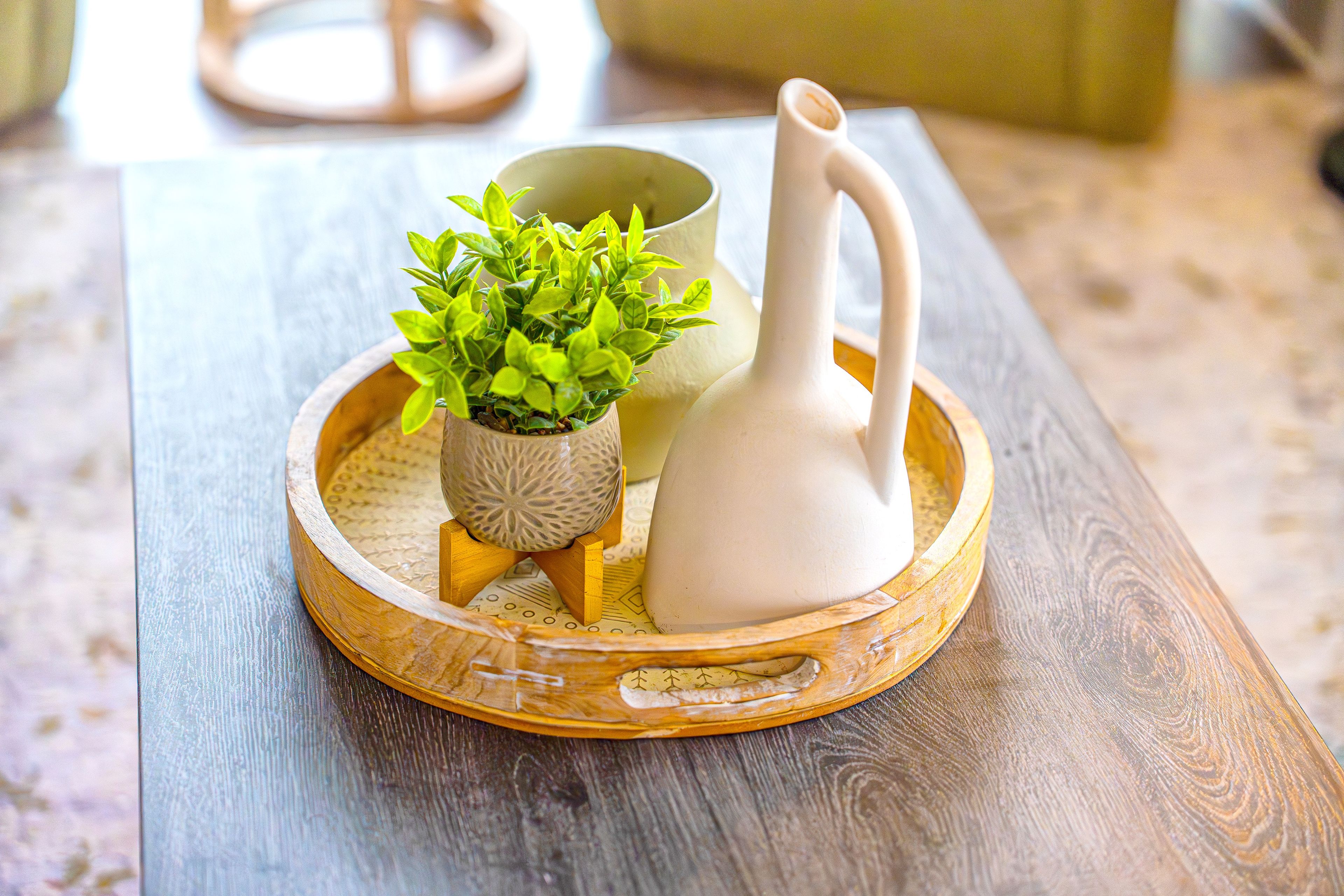 A wooden tray with a small potted plant and a white pitcher on a wooden table.