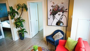 Un salon avec un canapé rouge, un fauteuil bleu, une table basse en bois ornée d’une plante et un tapis aux couleurs vives.