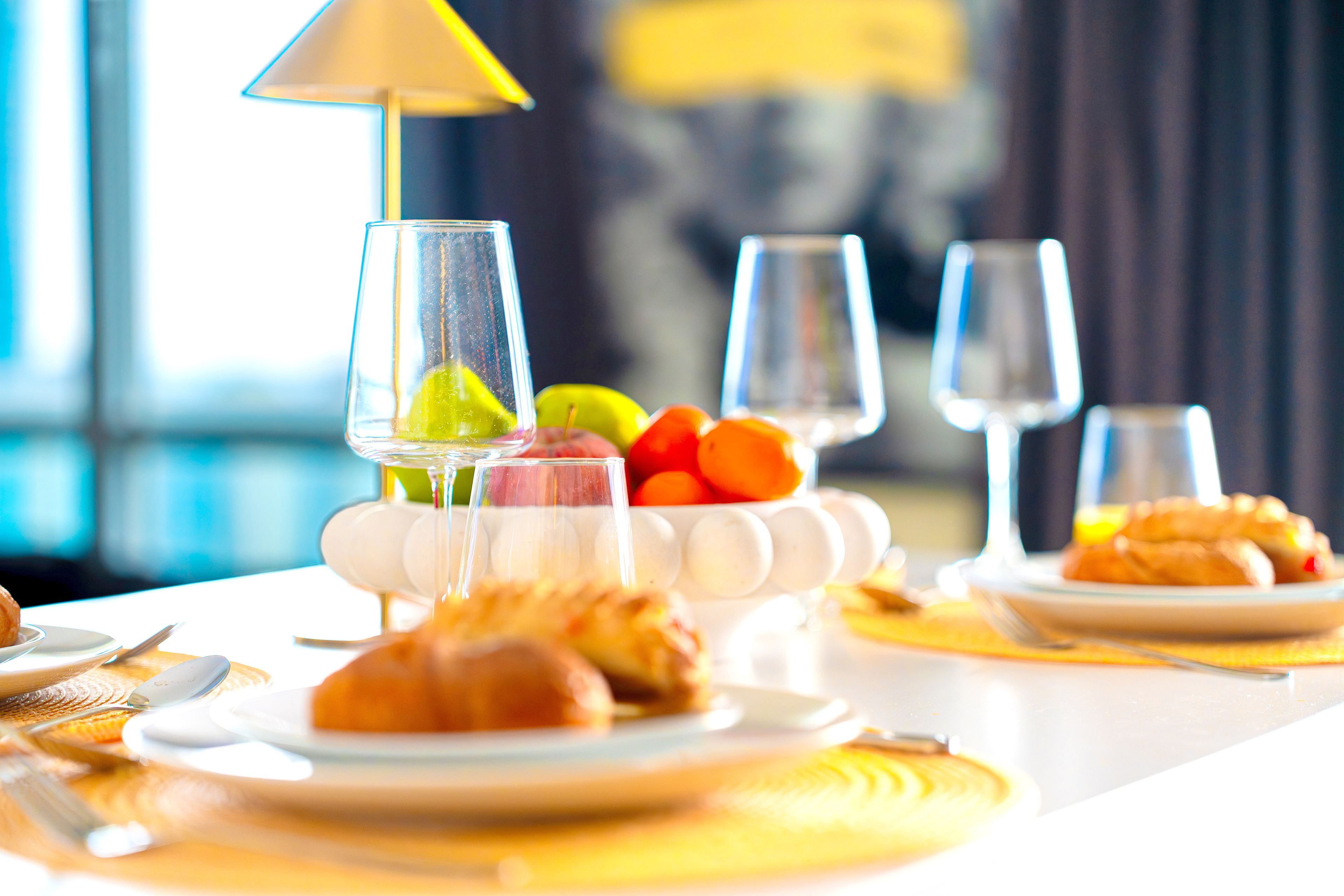 A dining table with plates of food, glasses of water, and a fruit bowl.