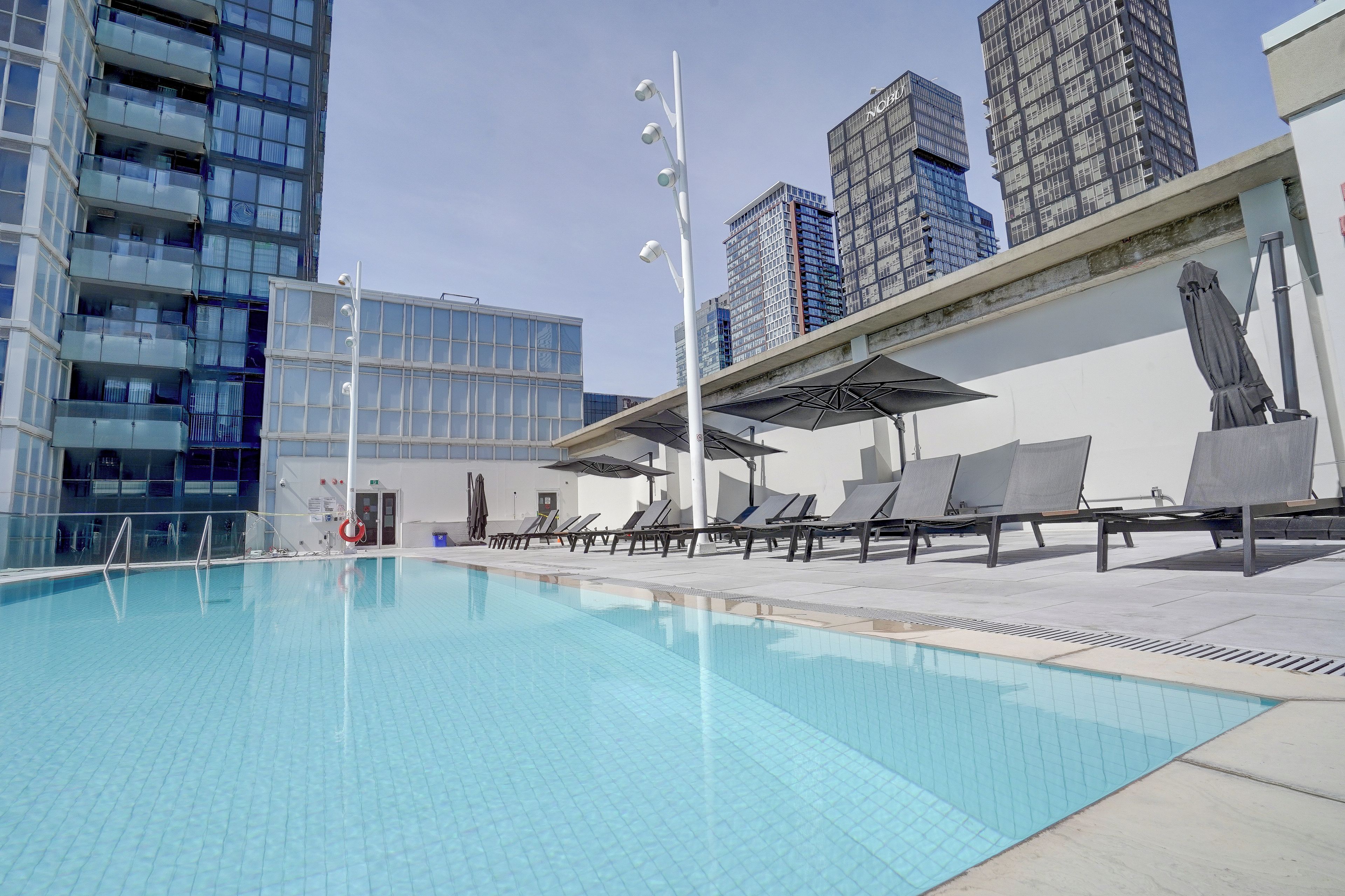 A swimming pool with lounge chairs and umbrellas, surrounded by modern buildings.