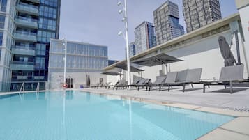 A swimming pool with lounge chairs and umbrellas, surrounded by modern buildings.