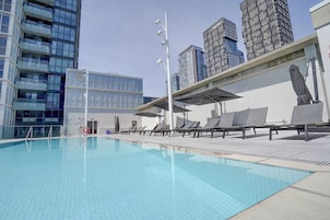 Piscina com espreguiçadeiras e guarda-sóis, cercada por edifícios modernos.