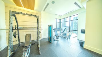 Un gimnasio con equipo de levantamiento de pesas, una banca y una ventana con vista a la ciudad.