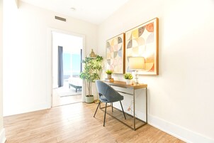A room with a desk, chair, lamp, and wall art.