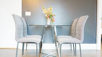 A modern dining area with two upholstered chairs, a glass table, and a vase with flowers.