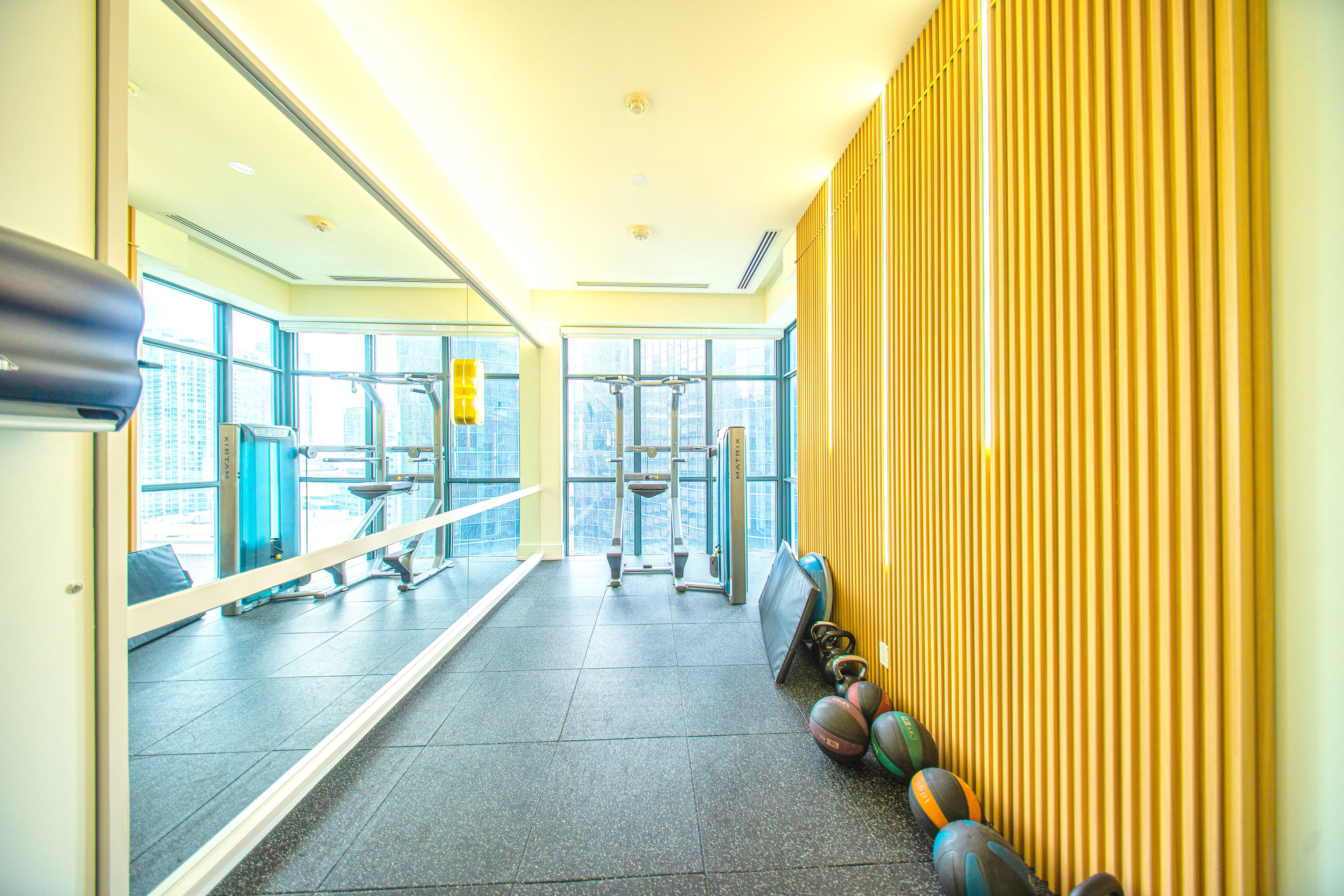 A gym with exercise equipment, a large mirror, and a view of the city through large windows.