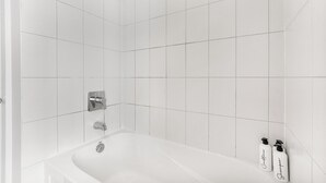 A white bathroom with a bathtub, a showerhead, and two bottles of shampoo.