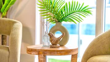 A round wooden table with a vase of green foliage, a glass bottle, and a bird-shaped object.