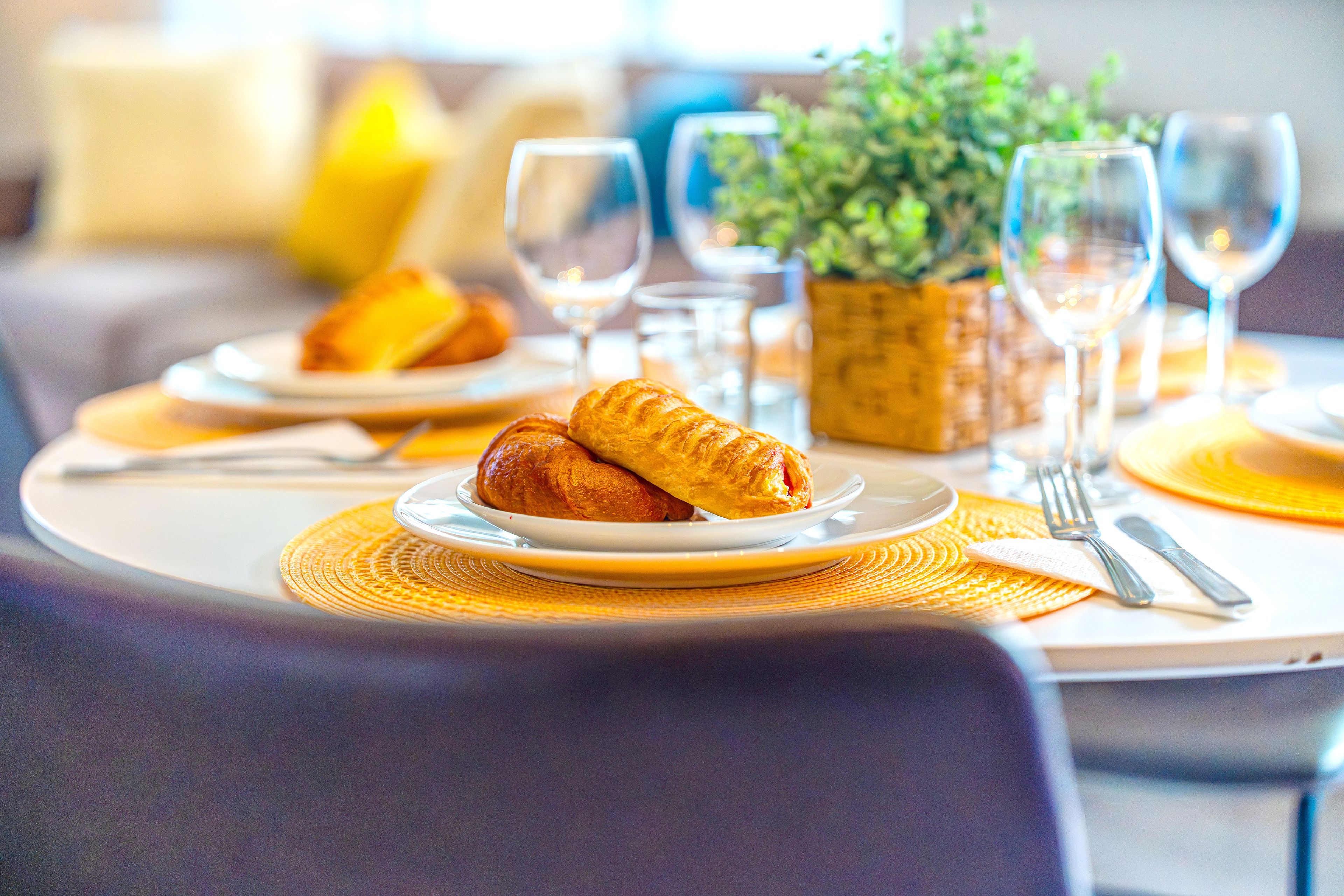 A dining table with plates, croissants, wine glasses, and cutlery.