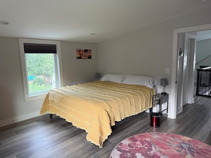 Ein Schlafzimmer mit Bett, Fenster, Gemälde, Nachttisch und einer Treppe.