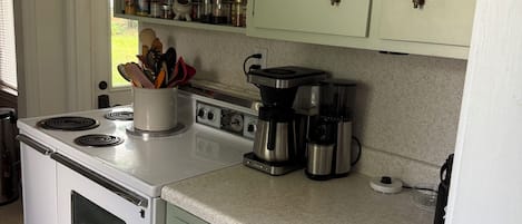 A kitchen with a white stove, a coffee maker, and green cabinets.