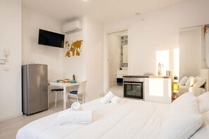 Ein Hotelzimmer mit Bett, Schreibtisch, Fernseher, Kühlschrank und einer Küchenzeile.