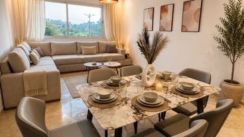A modern dining area with a marble table, grey upholstered chairs, and a red pendant light.