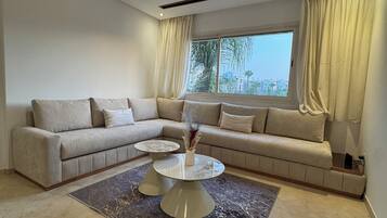 A modern living room with a sectional sofa, a round coffee table, and a large window with curtains.