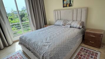 A bedroom with a bed, a nightstand, a painting, and a view through a window.