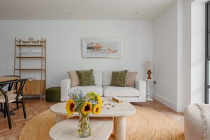 A living room with a white sofa, a coffee table, a vase with sunflowers, a wooden side table, and a framed picture on the wall. - One bedroom apartment near beach and Westbourne (Bournemouth)