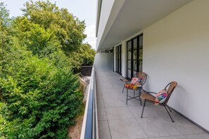 Ein Balkon mit zwei Korbstühlen, einem Blumentopf und einem Tisch mit einem Getränk.