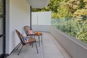 Un balcon avec deux fauteuils en osier, une petite table avec des éléments pour le petit-déjeuner et une vue sur un jardin.