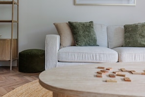 Ein Wohnzimmer mit Sofa, Hocker und Couchtisch, auf dem Spielzeug verstreut liegt.