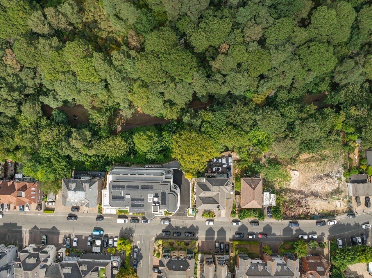 Eine Vogelperspektive eines Wohngebiets mit einem großen Gebäude, Parkplätzen und umliegender Bepflanzung.