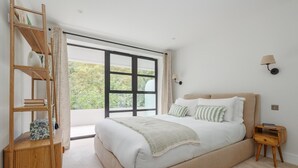 Un dormitorio con una cama grande, una estantería de madera, una mesita de noche y una ventana con vistas a zonas verdes.