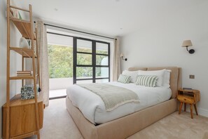 Ein Schlafzimmer mit einem großen Bett, einer Holzregal, einem Nachttisch und einem Fenster mit Blick auf Grünflächen.