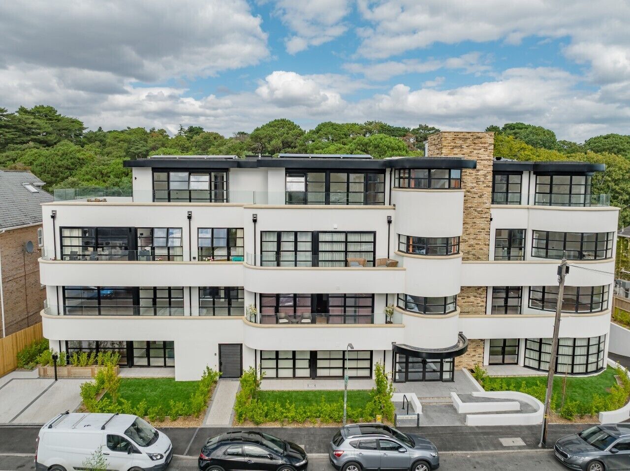 Un edificio residencial de varios pisos con balcones, ventanas amplias y un estacionamiento al frente.