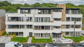 Un edificio residencial de varios pisos con balcones, ventanas amplias y un estacionamiento al frente.