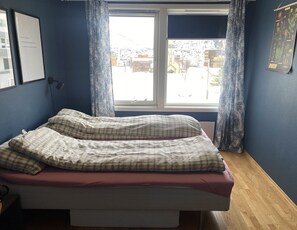 A bedroom with a bed, a window with curtains, a wall-mounted lamp, and a framed picture. - Apartment in the middle of Tromsø City (Tromsø)