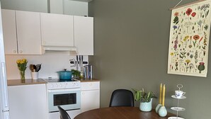 Uma sala de jantar com uma mesa e cadeiras de madeira, uma cozinha ao fundo e uma ilustração botânica na parede.