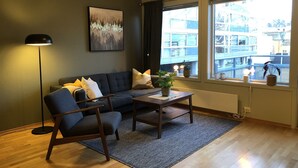 Uma sala de estar moderna com sofá, poltrona e mesa de centro, um abajur e um quadro na parede.