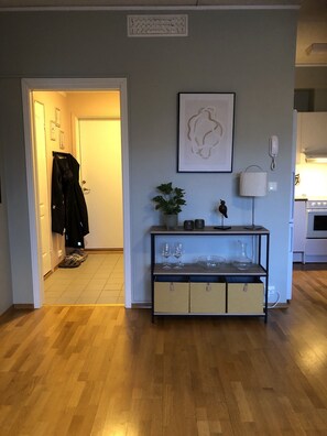 A hallway with a coat rack, a framed abstract artwork, a potted plant, a bird sculpture, and a glass cabinet with wine glasses. - Apartment in the middle of Tromsø City (Tromsø)
