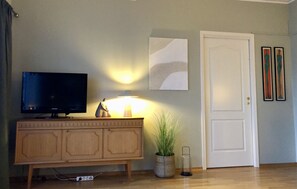 A room with a television on a wooden cabinet, a lamp, a door, and two framed artworks on the wall. - Apartment in the middle of Tromsø City (Tromsø)