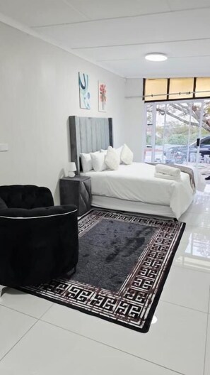 Habitación de hotel con una cama, una silla negra, una alfombra y una ventana con vistas.