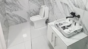 Un baño con cabina de ducha de vidrio, inodoro blanco y tocador de mármol con lavamanos y espejo.